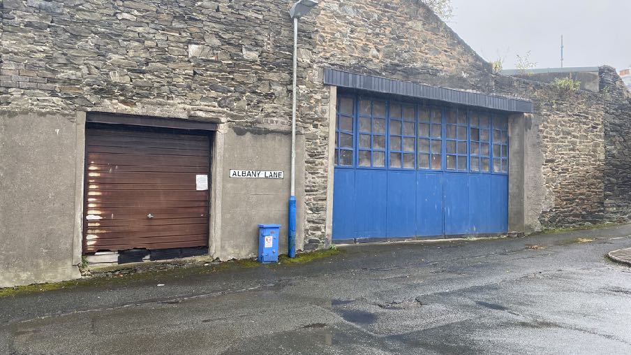 A street-level photograph showing a stone building with two large garage doors, one brown and one blue, located on Albany Lane.