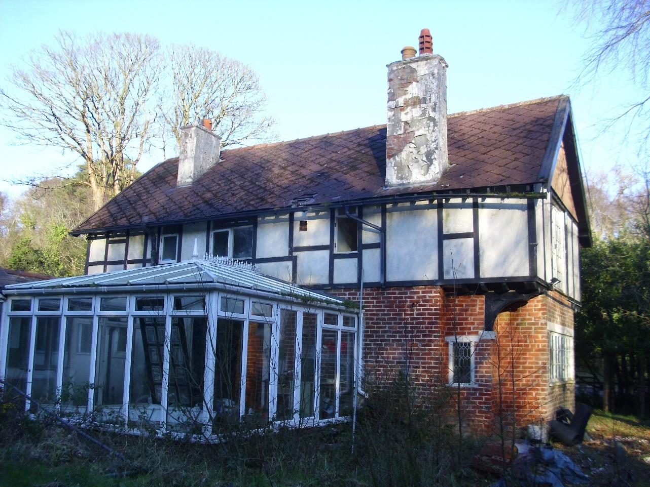 A photograph of a two-story residential property featuring mock-Tudor upper cladding and a large white conservatory extension attached to the front.