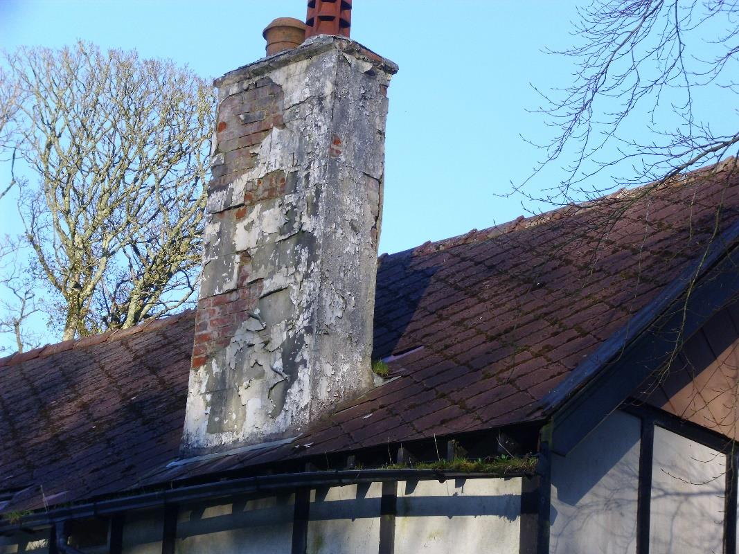 A close-up photograph showing a weathered brick chimney stack with peeling white render and terracotta pots on a tiled roof.