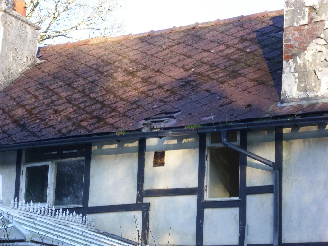 A photograph showing the upper facade and roofline of a timber-framed building with tiled roofing, chimneys, and visible guttering.