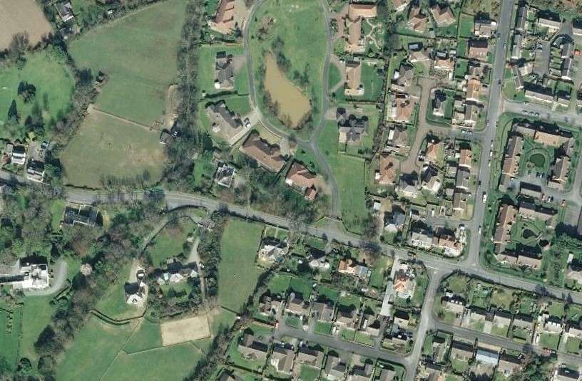 An aerial photograph showing a mix of residential housing and green fields, likely serving as a location map for the site.