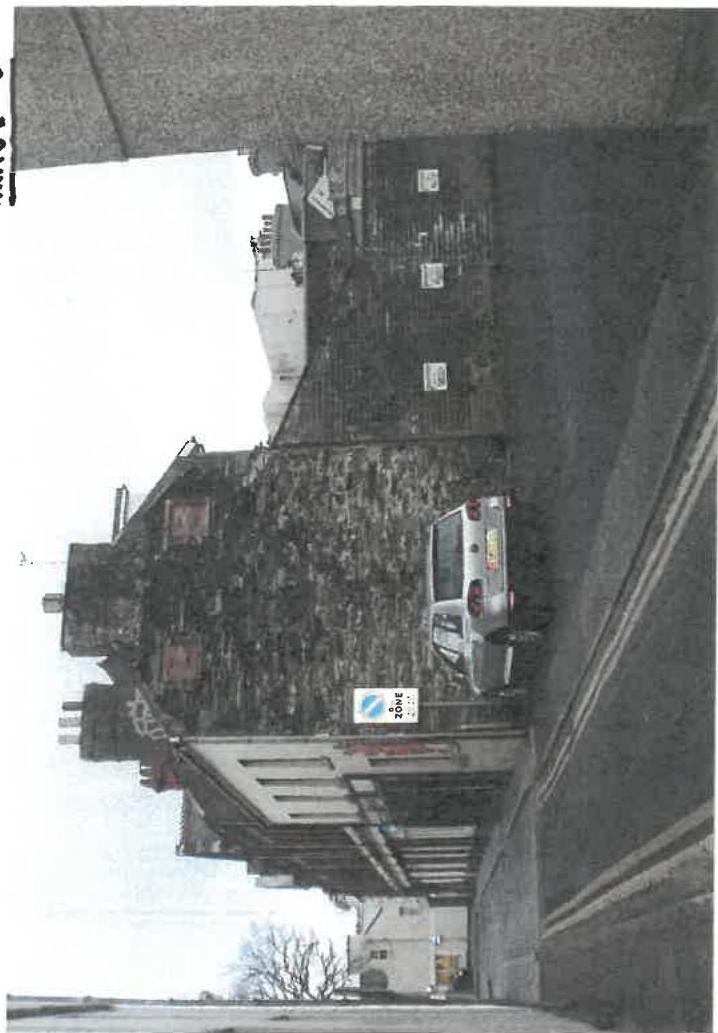A rotated photograph showing the exterior of a stone building, likely a shop, with a car parked on the street.