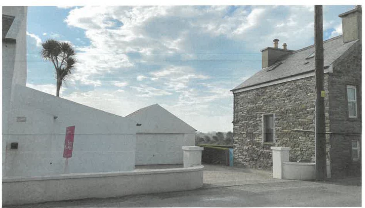 Exterior photograph showing a white garage structure adjacent to a stone house with a driveway and boundary walls.