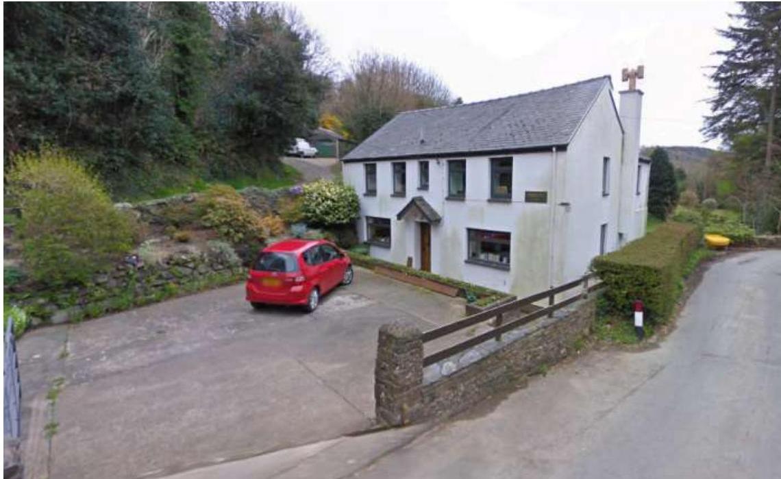 A photograph showing a white two-story detached house with a slate roof and a concrete driveway.