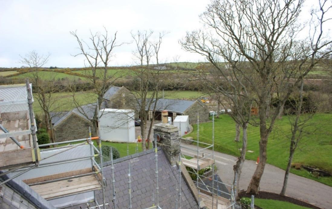A high-angle photograph taken from scaffolding overlooking a rural property with stone buildings, a driveway, and green fields.
