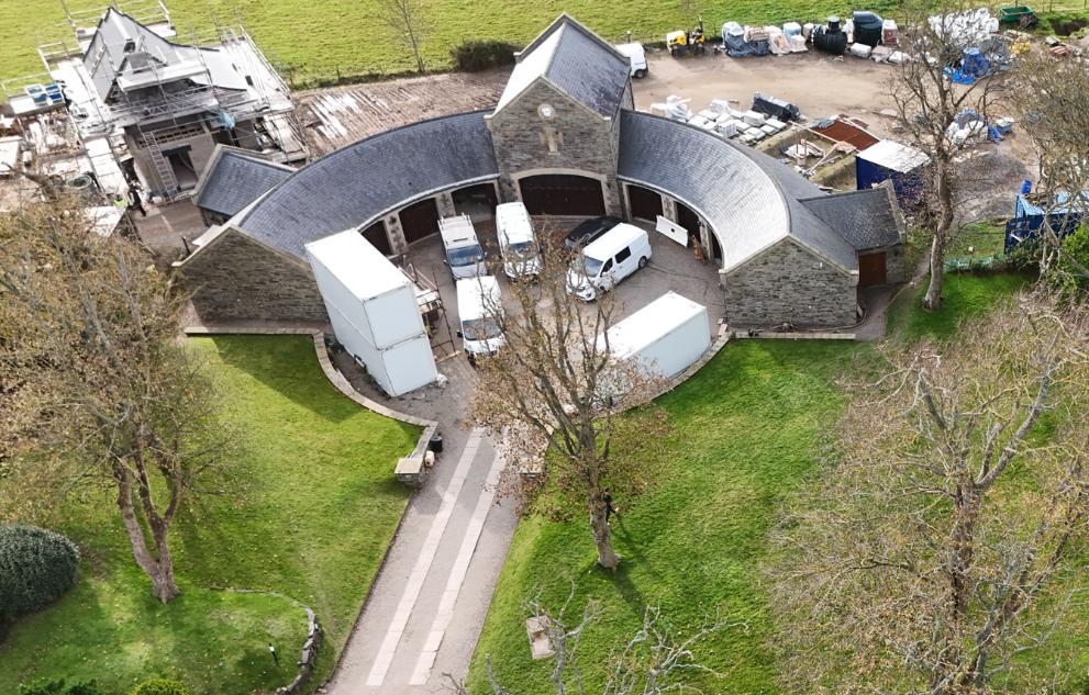 Aerial photograph showing a large curved stone building complex with several white vans parked inside and construction scaffolding on an adjacent structure.