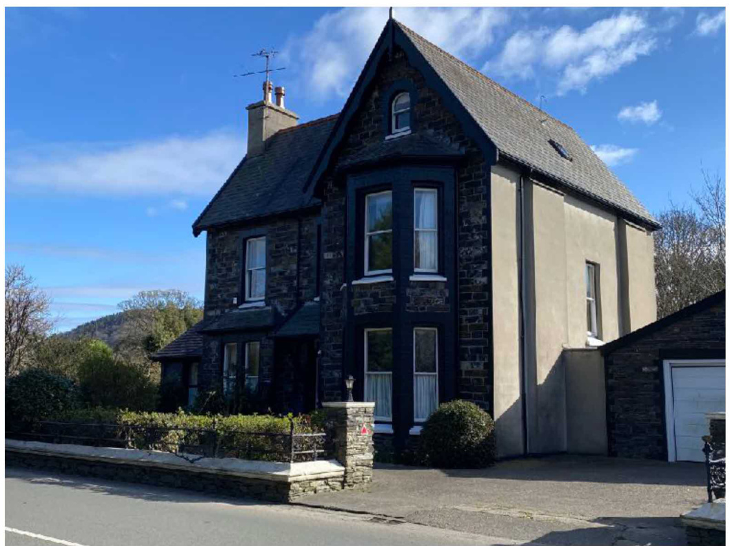 A photograph of a two-story detached stone house featuring a rendered side elevation and an attached garage.