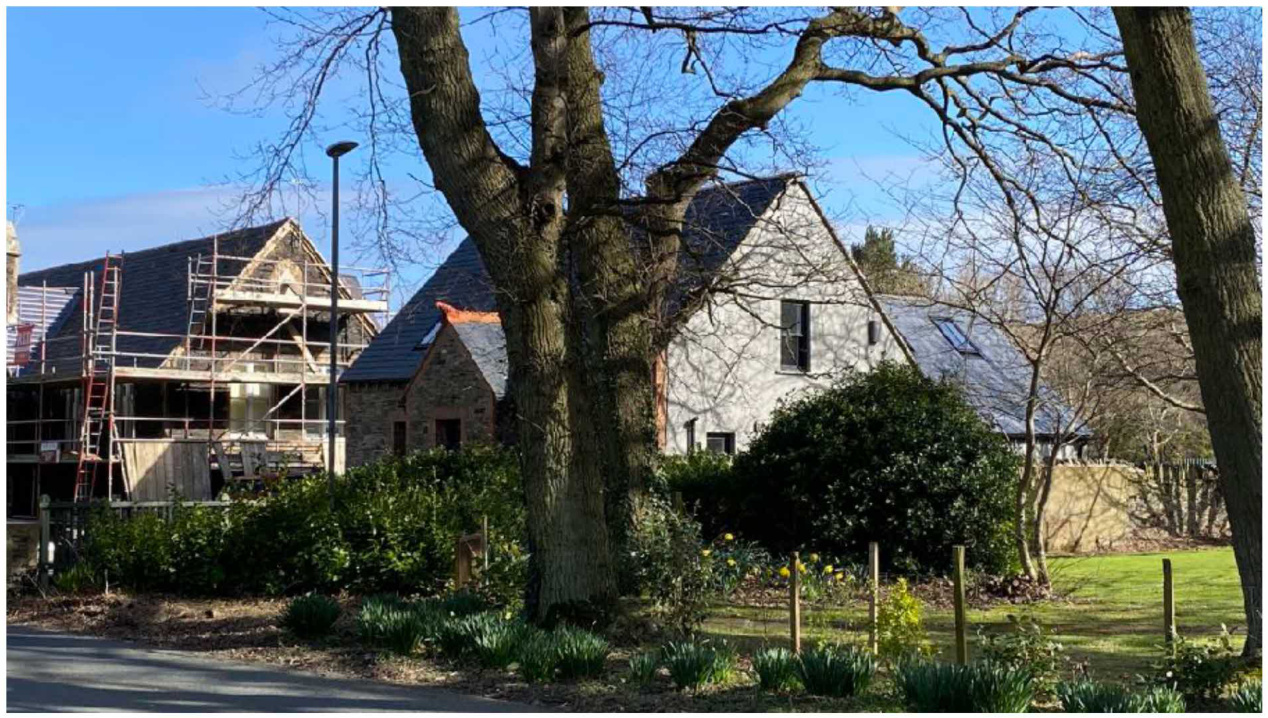 A photograph showing a rural property with a building under construction featuring scaffolding alongside an existing white-washed house.