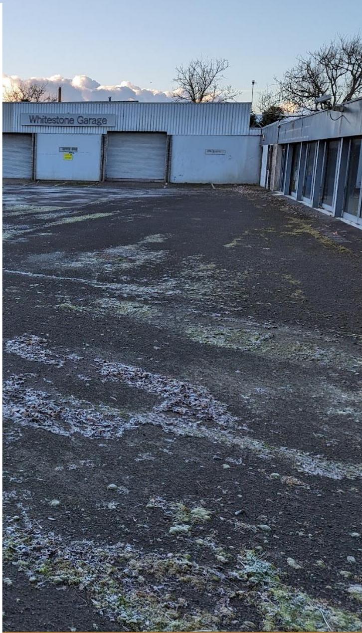 A photograph showing the exterior of a commercial property labeled 'Whitestone Garage' with roller shutter doors and a paved forecourt.