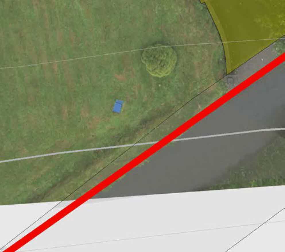 An aerial site plan showing a grassy plot of land adjacent to a road, marked with a prominent red boundary line.