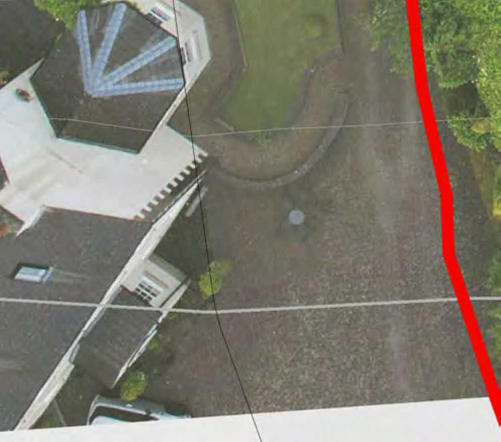 An aerial view of a detached property showing the house, driveway, and surrounding land with a red boundary line marked on the right side.