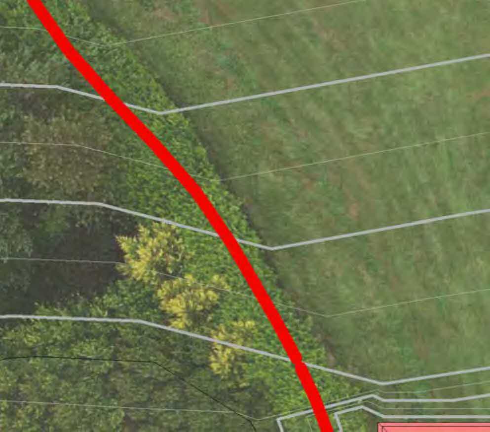 An aerial view of a grassy plot with trees, overlaid with white boundary lines and a prominent red diagonal line, indicating a site plan.