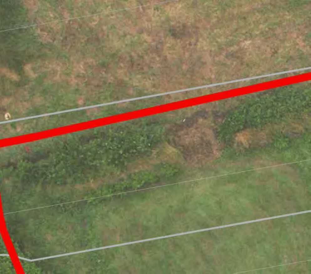 An aerial view of a grassy plot of land with red and white lines overlaid, indicating site boundaries or survey lines.