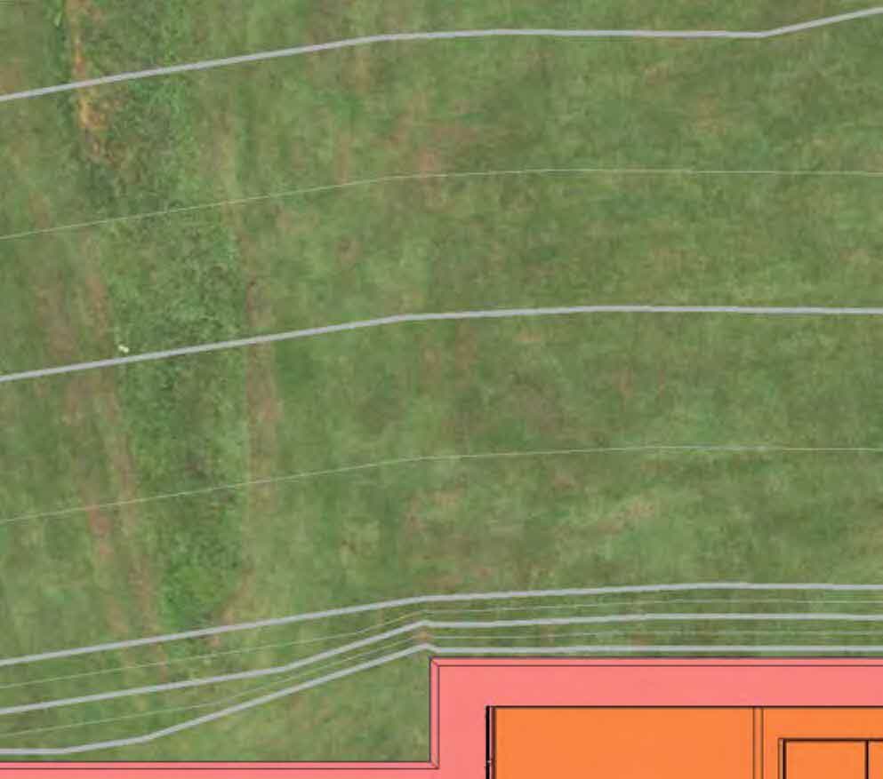 The image shows a site plan overlaid on an aerial view of a grassy field, featuring contour lines and the colored footprint of a proposed building extension in the bottom right corner.