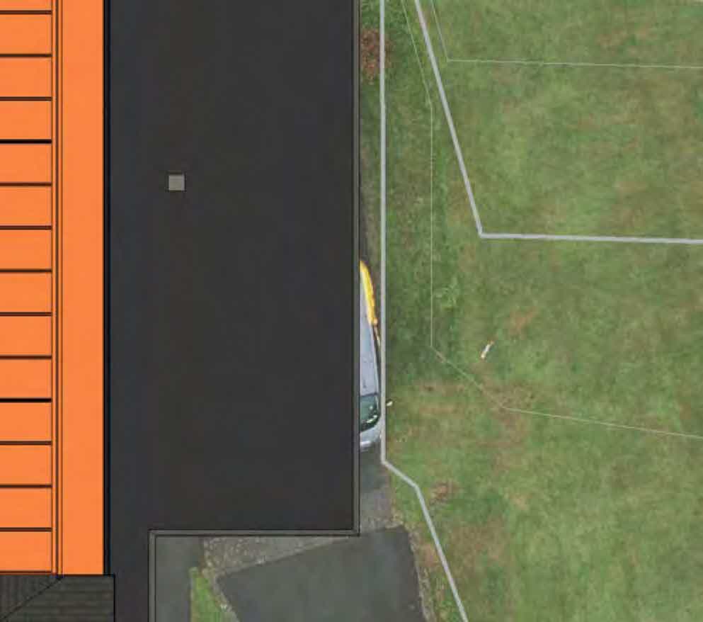 Aerial view showing a building with orange cladding adjacent to a grassy field with white lines.