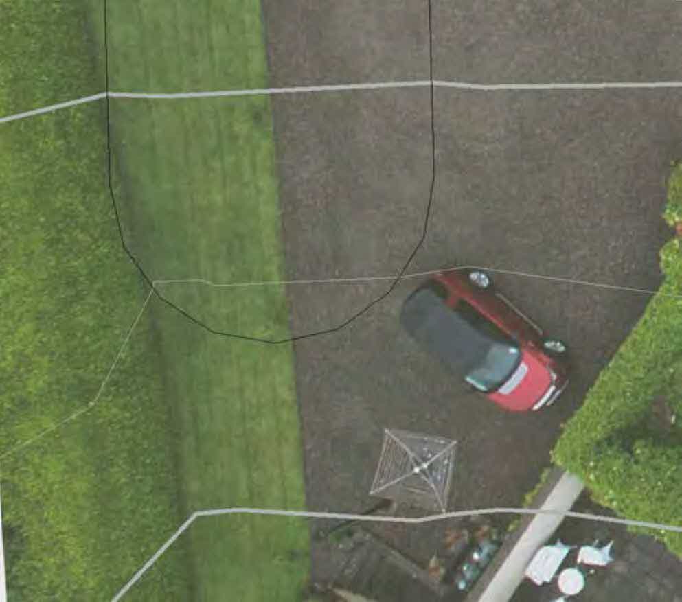 Aerial site plan showing a driveway with a red car, grassy area, and white boundary lines overlaid with a black outline indicating a proposed structure.