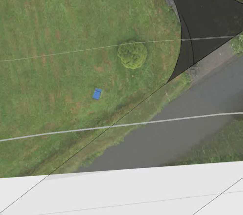 An aerial view of a grassy plot of land with white boundary lines overlaid, showing a tree and a road.