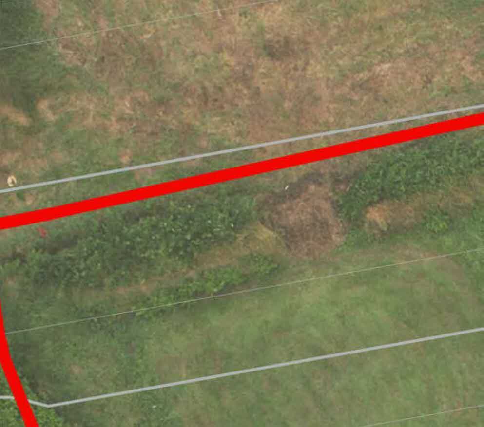 An aerial view of a grassy plot of land with red and white boundary lines overlaid.