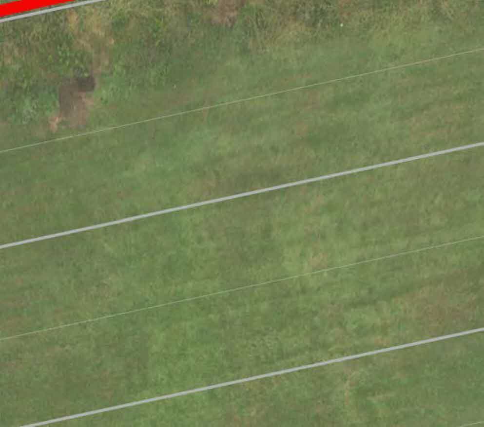 Aerial view of a grassy field with faint white survey or boundary lines overlaid, likely a section of a site location map.