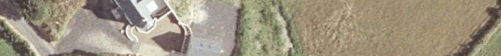 An aerial view showing a house with a driveway and a large adjacent field or agricultural land.