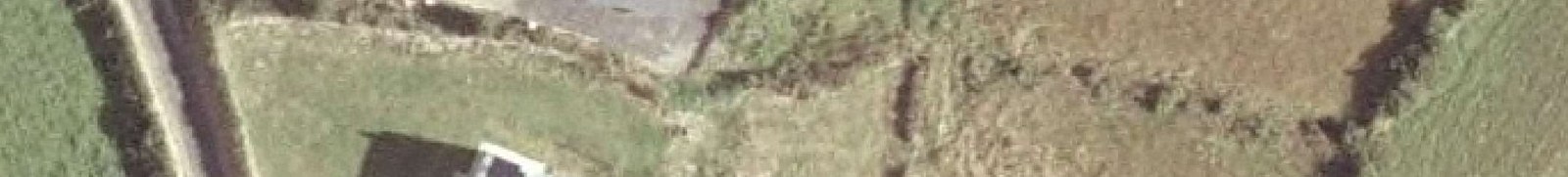 Low resolution aerial image showing a rural property site with a building, road, and fields.