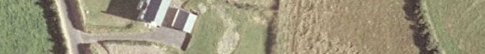 An aerial view showing a building with a driveway and surrounding grassy fields.