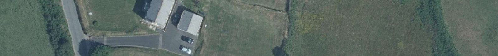 An aerial satellite view of a rural property featuring a detached house and separate garage with a driveway containing parked cars.