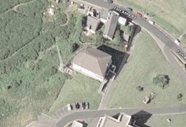 An aerial satellite view of a property on Fort Anne Road showing a detached house, driveway with parked cars, and surrounding greenery.
