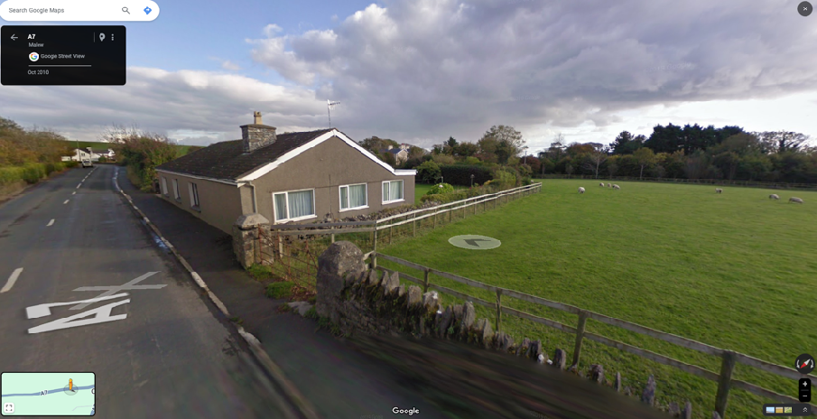Google Street View screenshot showing a detached bungalow alongside the A7 road with a sheep pasture to the right.