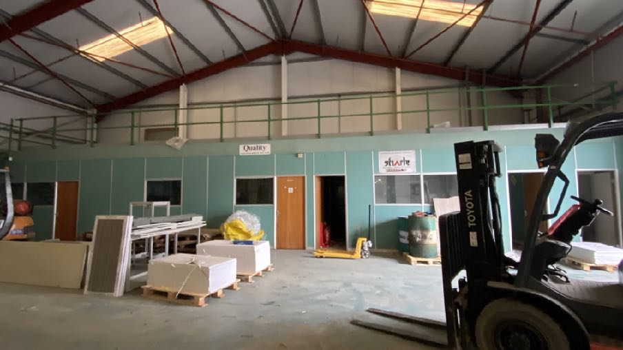 Interior photograph of an industrial unit featuring a mezzanine level, partitioned office area with signage, and industrial equipment like a forklift.
