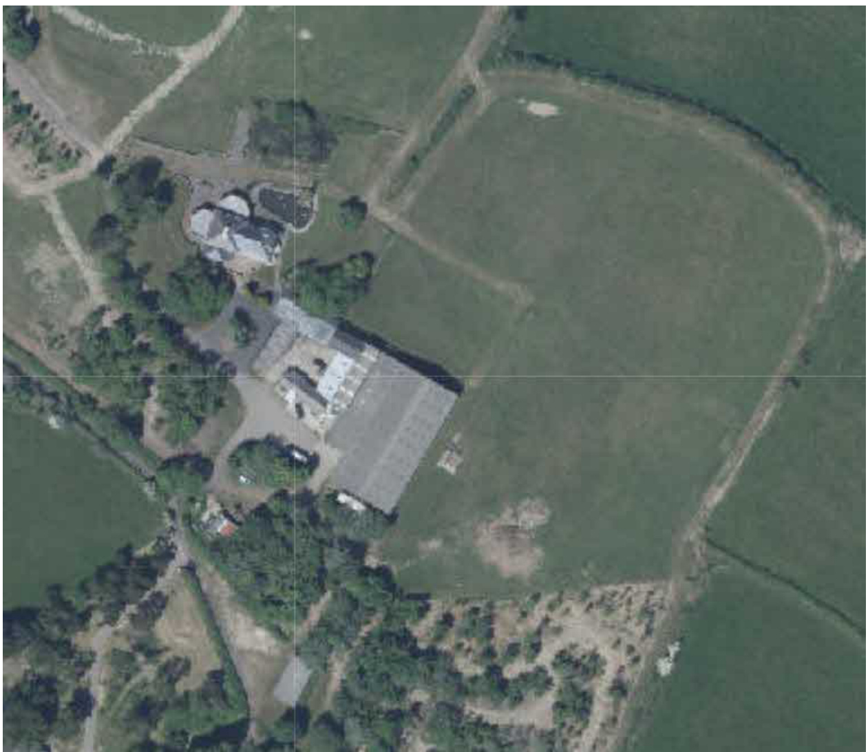 An aerial view of a rural property showing a large grey-roofed building, surrounding green fields, and dirt access tracks.