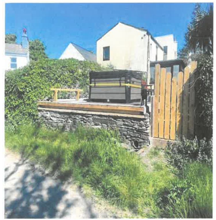A photograph showing a wooden deck raised on a stone wall with a large enclosure on top, alongside a new wooden fence and gate.