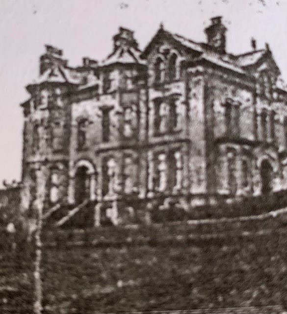 A grainy black and white photograph showing the exterior of a large, multi-story stone building with a complex roofline and multiple chimneys.