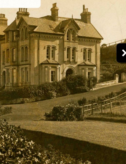 A sepia-toned photograph showing a large, detached house with a complex roofline, multiple chimneys, and arched windows situated on a sloping site.