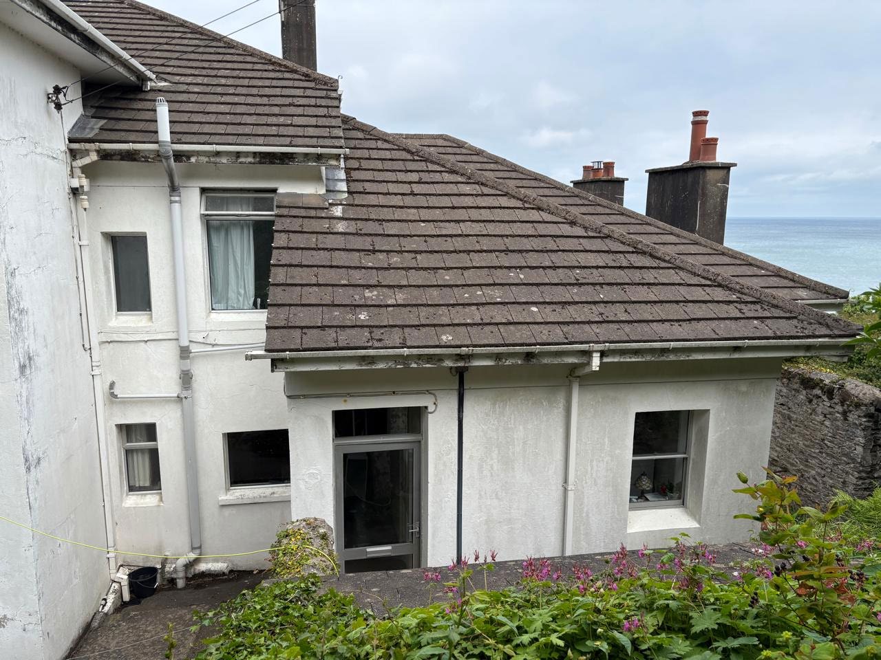 A photograph showing the rear elevation of a white-rendered residential property with a tiled roof and chimneys, overlooking the sea.