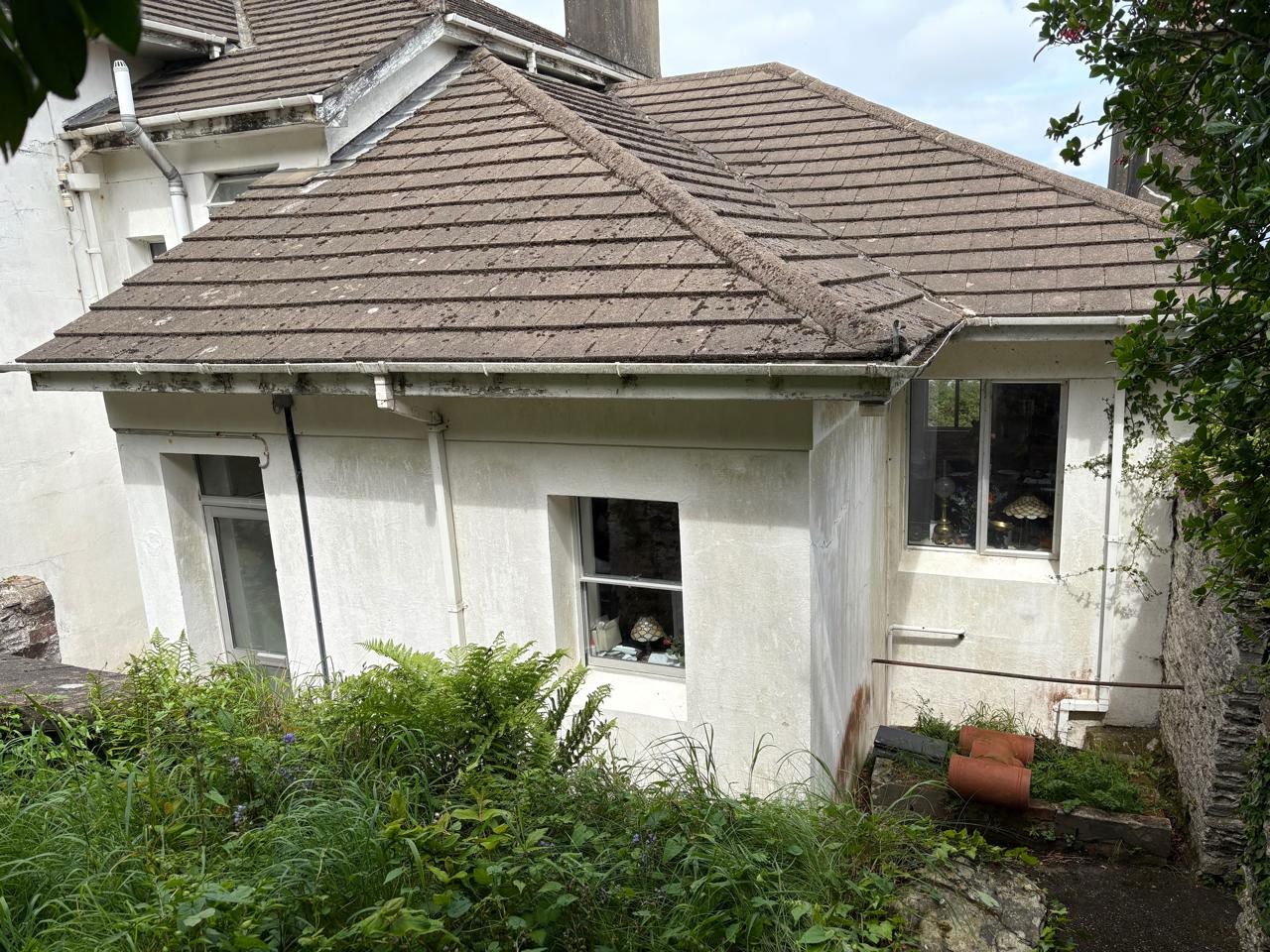 A photograph showing the exterior roof and upper walls of a white residential building with tiled roofing and guttering.