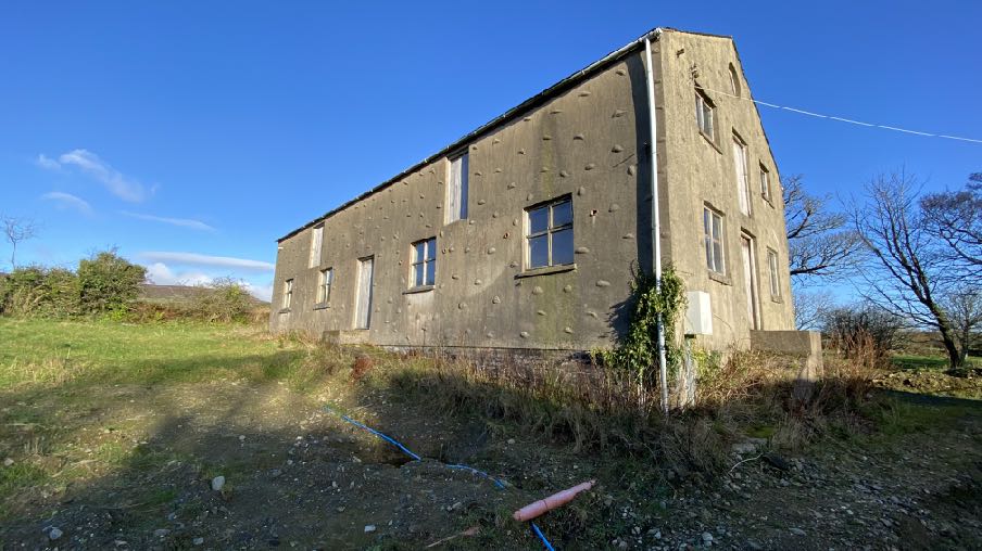A photograph of a large, rectangular concrete outbuilding situated in a grassy rural field under a clear blue sky.