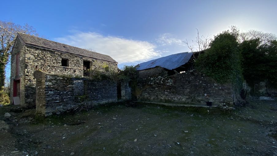A photograph showing a rural site with a two-story stone outbuilding and a lower ruined wall structure.