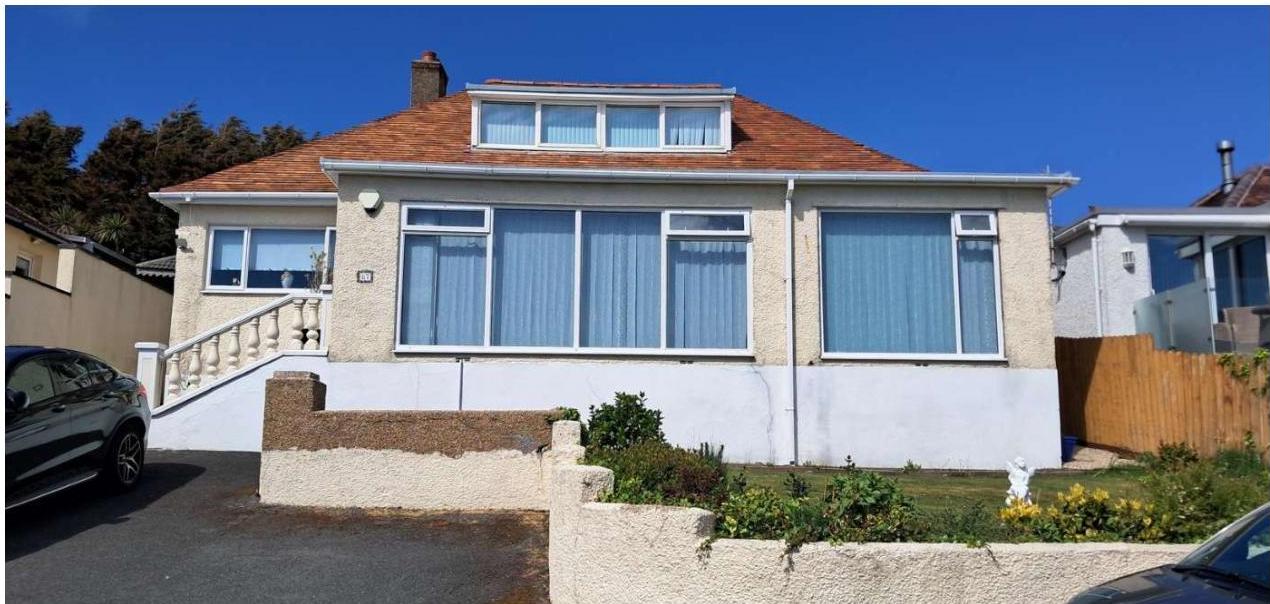 A photograph of a detached bungalow featuring a tiled roof, dormer window, and a driveway with steps leading to the entrance.