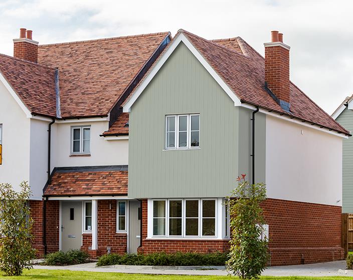 A photograph of a two-story detached house featuring a mix of red brick, white render, and light green vertical cladding on the gable end. The property has white uPVC windows, a tiled roof, and brick chimneys.