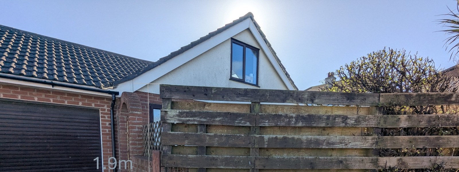 A photograph showing the side elevation of a residential property featuring a garage door and a wooden fence in the foreground.