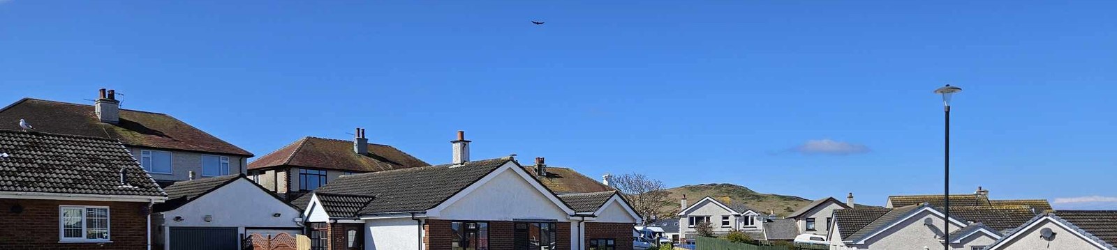 A panoramic photograph showing a row of residential houses with pitched roofs under a clear blue sky, likely depicting the street context for the application.