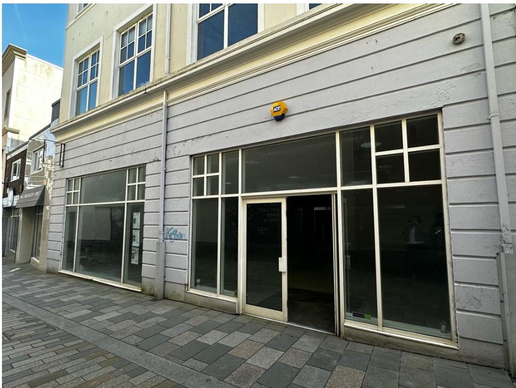 Street-level photograph of a vacant commercial retail unit featuring large plate glass windows and a central entrance door.