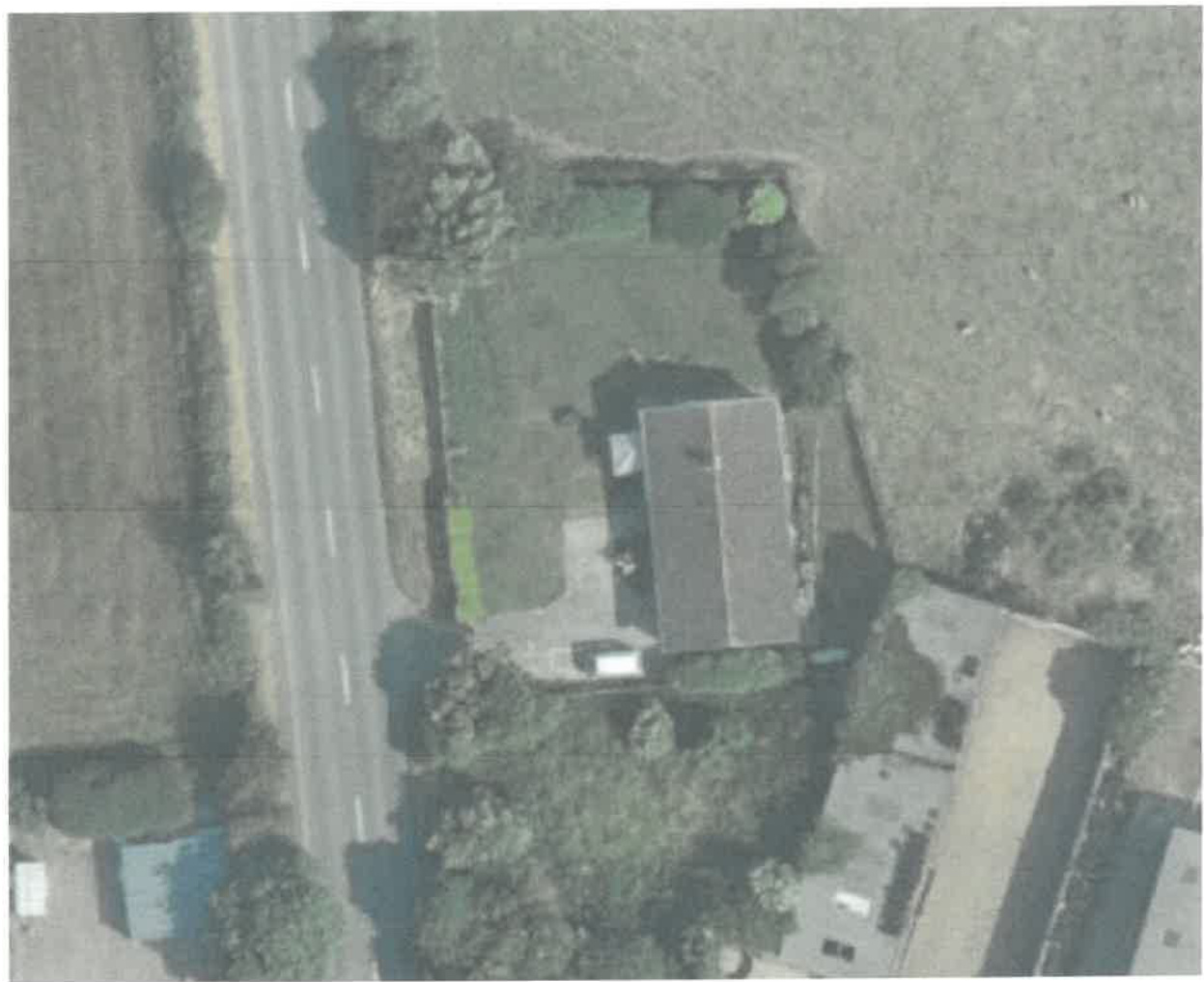 An aerial photograph showing a rural property with a detached bungalow, driveway, and surrounding fields adjacent to a road.