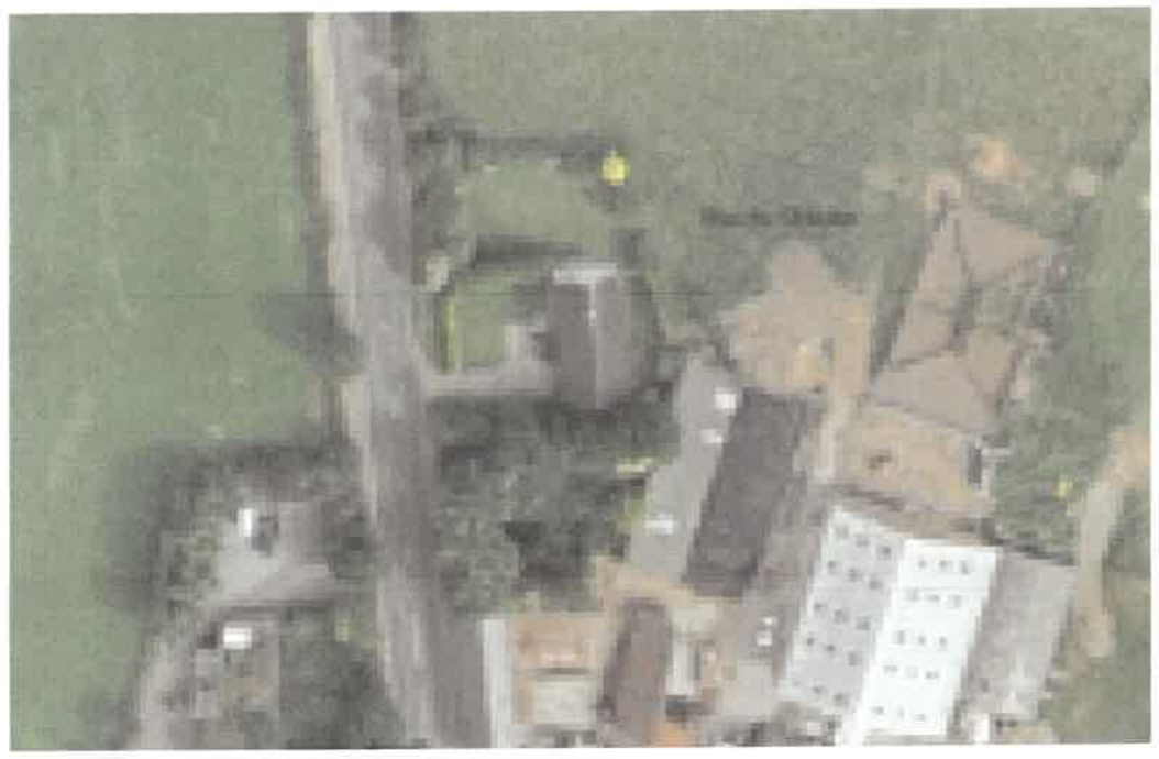 A low-resolution aerial site plan showing a road, surrounding green fields, and nearby buildings with yellow markers indicating the application area.