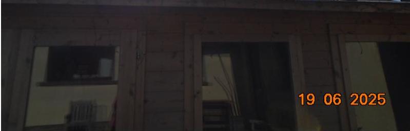 A dimly lit photograph showing the wooden exterior wall of a building with windows and an orange date stamp.