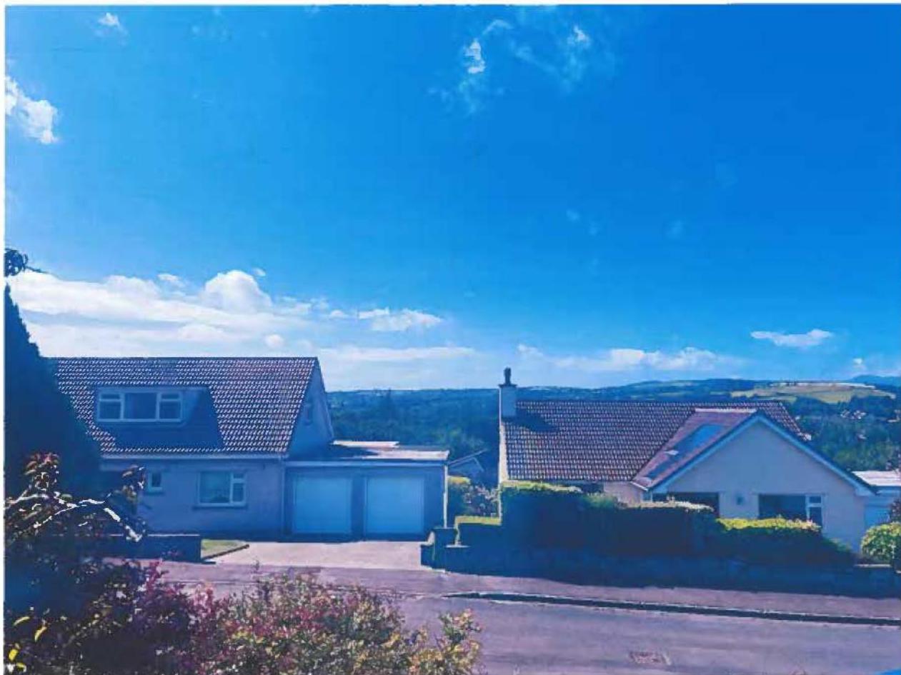 A photograph showing two detached houses with a double garage on the left, set against a backdrop of rolling hills and a blue sky.