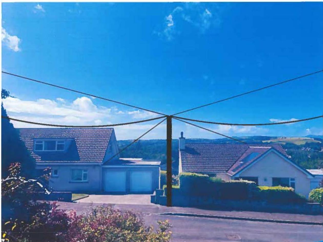 A photograph showing a residential street scene with detached houses, a wooden utility pole with overhead wires, and a blue sky.