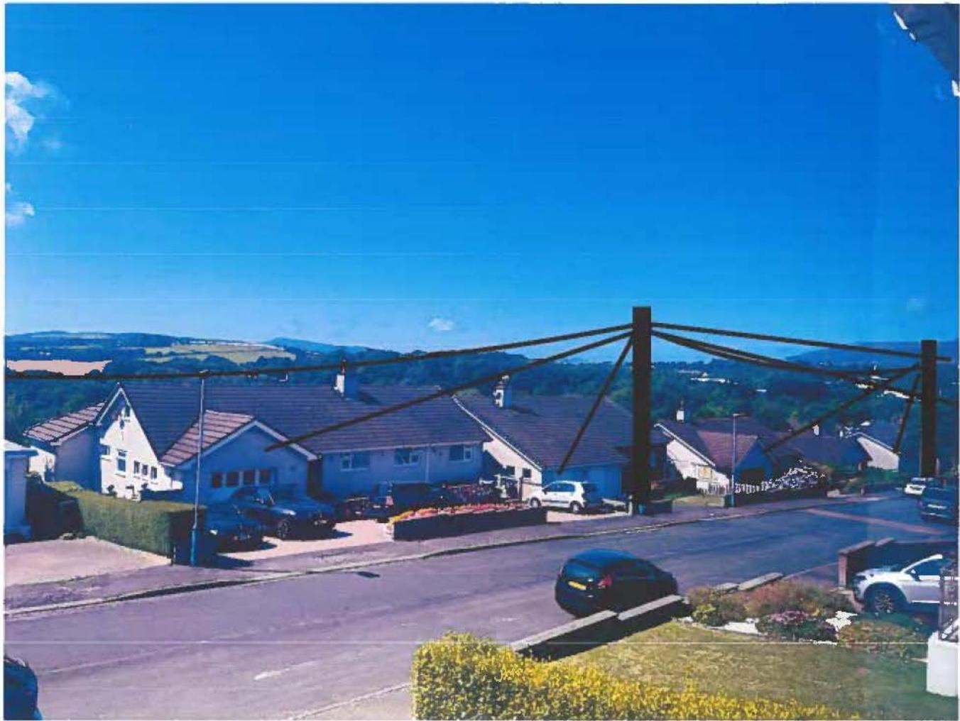 A photograph showing a residential street with houses and large wooden telegraph poles in the foreground against a blue sky.
