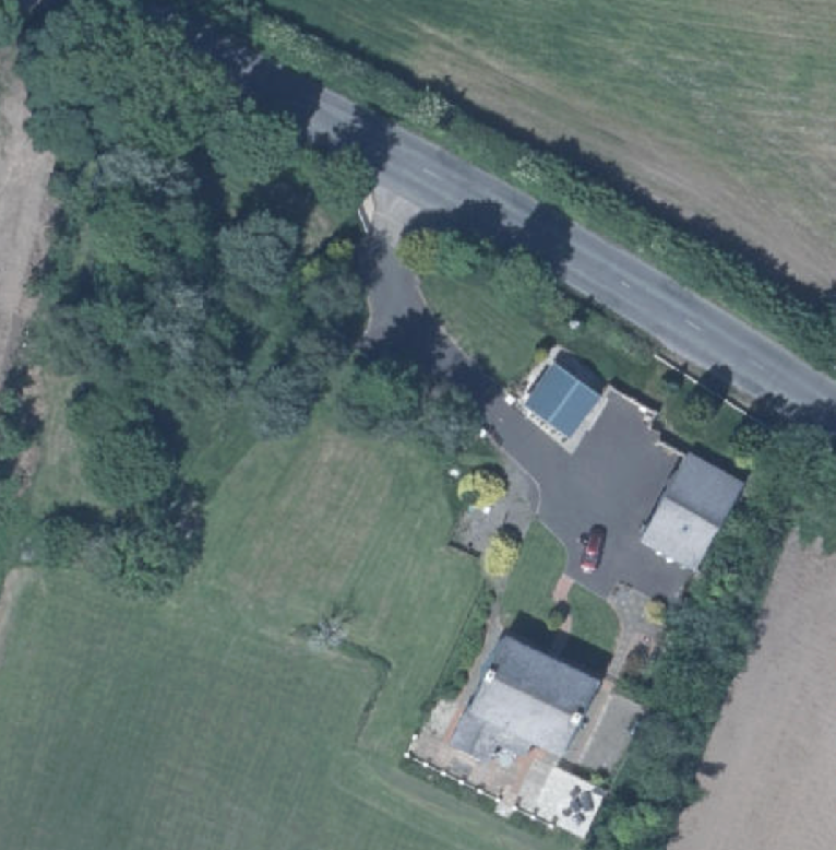 Aerial satellite view of a rural property showing a house, driveway, and outbuilding with solar panels.